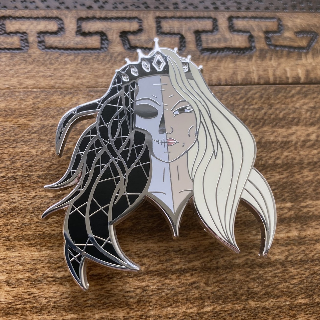 Silver-plated enamel pin of the Norse god Hel. The pin depicts the icon as half corpse and half alive. Angle shows off the sliver-plating.