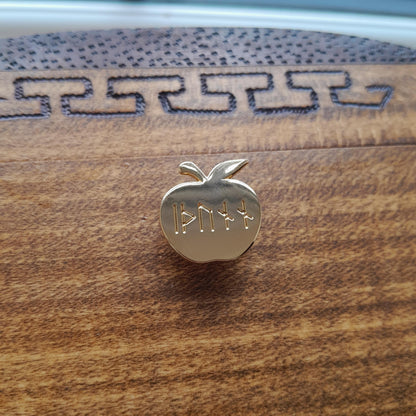 Enamel pin of Idunn's golden apple. Engraved on the apple is the word idunn in younger futhark. Angle shows off the gold plating.