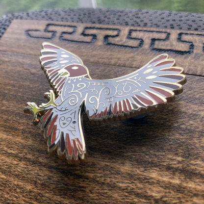 Gold-plated enamel pin of the Norse god Freyja. Pin contains knotwork and is depicted as a falcon. Angle shows off gold-plating.