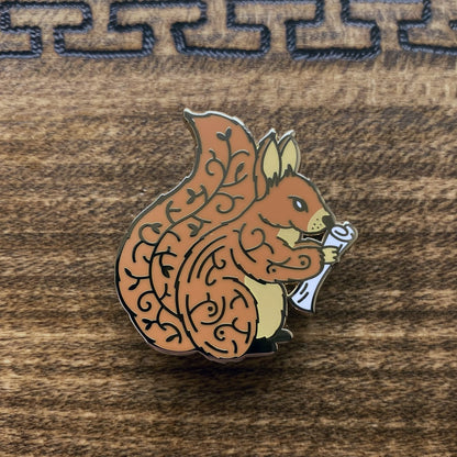 Gold-plated enamel pin of Norse icon Ratatoskr. The pin contains imagery of the world tree and is depicted as a squirrel holding a rolled up paper.