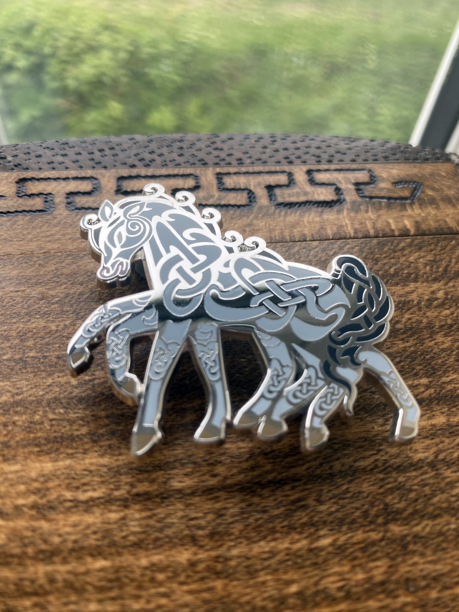 Silver-plated enamel pin of the Norse icon Sleipnir. Pin contains knotwork and is depicted as a eight-legged horse. Angle shows off the silver-plating.