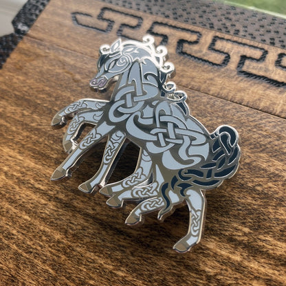 Silver-plated enamel pin of the Norse icon Sleipnir. Pin contains knotwork and is depicted as a eight-legged horse. Angle shows off the silver-plating.