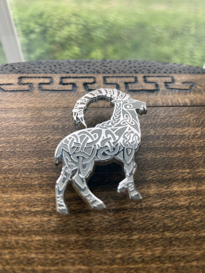 Norse god Thor, depicted as a goat enamel pin. The pin is silver plated and contains knotwork. Pin is at an angle to show off silver plating.