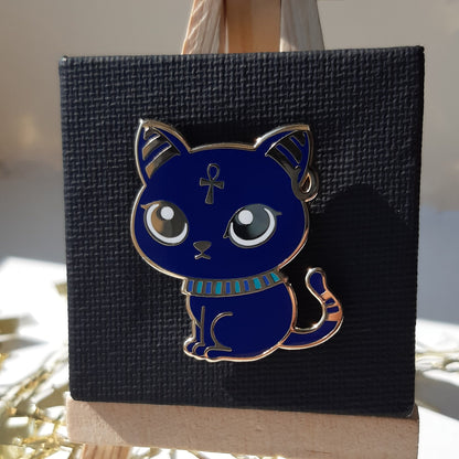 Gold-plated enamel pin of the Egyptian god Bastet, depicted as a blue cat. Pin contains ancient egyptian symbols. Angle shows off gold-plating.